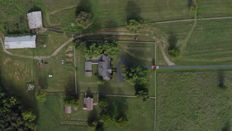 Top-down-aerial-over-fenced-farmhouse-with-barn-and-tractor-in-backyard,-4K