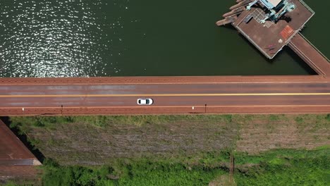 Aerial-drone-view-of-a-single-vehicle-crossing-a-dam-of-a-reservoir-through-which-a-tropical-highway-passes-in-Misiones,-Argentina