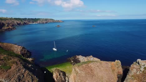 Die-Felsige-Insel-Sark-Per-Drohne-Erkunden,-Wo-Viele-Möwen-über-Ein-Einsames-Segelschiff-Hinwegfliegen