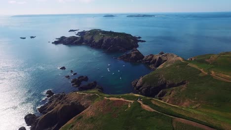 Aerial-drone-view-of-the-rocky-coast-and-the-Atlantic-Ocean-of-the-island-of-Sark-where-many-sail-boats-are-docked,-Channel-Islands