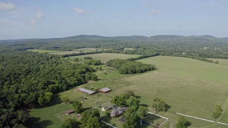 4k-wide-aerial-view-of-farmhouse-and-surrounding-fields-with-hills-in-distance