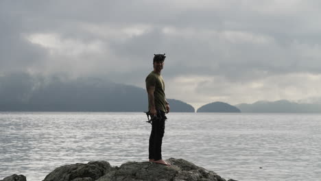 Caucasian-Man-With-FPV-Quadcopter-Standing-On-Rock-Overlooking-Calm-Sea-With-Overcast