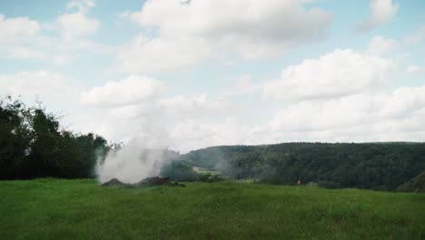 Pile-of-earth-on-large-green-field-with-white-smoke-moved-by-wind