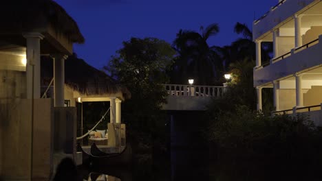 Stunning-tranquil-night-time-scene-of-small-tropical-bungalow's-along-a-small-river-with-a-illuminated-bridge-above-in-a-beautiful-exotic-vacation-resort-in-Riviera-Maya,-Mexico-near-Cancun-and-Tulum