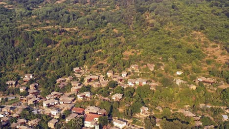 Slow-aerial-reveal-of-tree-coveed-hills-over-mountain-village-houses-of-Kovachevitsa-Rhodopes-Bulgaria