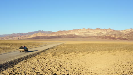 Follow-through-shot-of-SUV-on-road-amidst-hot-dry-barren-terrain-of-Death-valley-national-park