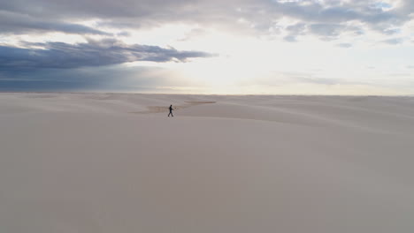 4K-aerial-of-silhouetted-man-walking-on-beautiful-white-sand-dunes-at-sunrise