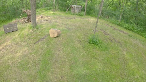 Aerial-view-slowly-moving-toward-a-log-cabin-style-outhouse-in-a-clearing-in-the-woods-with-scattered-stumps-and-logs