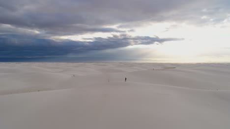 Orbiting-aerial-of-small-person-in-massive-white-sand-dune-field-sunrise,-4K