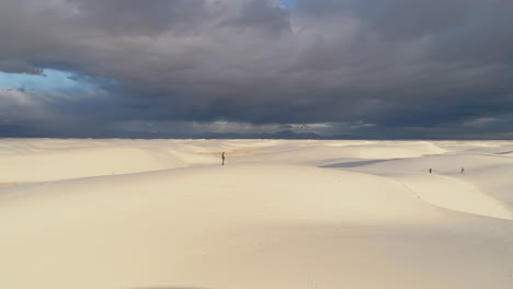 4K-aerial-of-man-standing-on-white-sand-dune-with-approaching-storm-in-distance