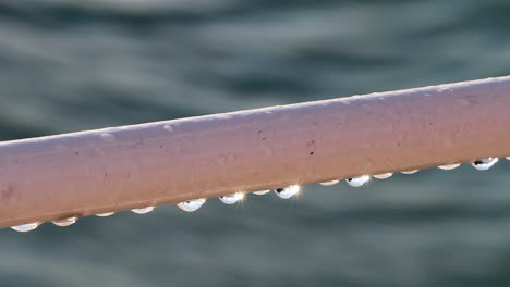Close-up:-Dew-drops-on-ship-railing-reflect-spectral-sunshine-on-water