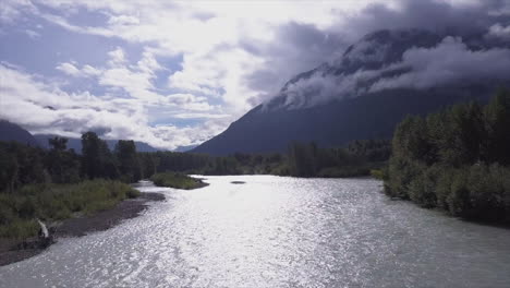 Silver-spectral-sunshine-reflects-on-Bella-Coola-river,-cloudy-valley