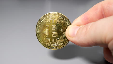 Gold-bitcoin-coin-held-between-fingers-in-hand-on-gey-table