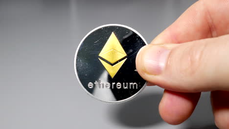Silver-and-ethereum-bitcoin-coin-held-between-fingers-in-hand-on-gey-table
