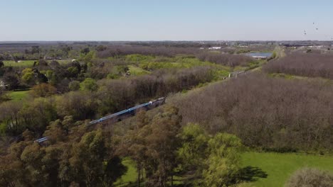 Blue-train-behind-trees-in-rural-area-of-Buenos-Aires,-Argentina