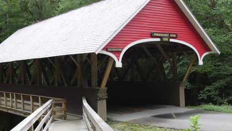 A-red-covered-bridge-sits-on-a-road-beside-a-wooden-walkway-in-front-of-a-forest