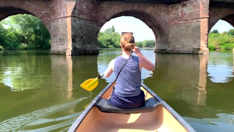 Girl-paddles-canoe-on-river-wye-through-stone-bridge-arch-in-the-sun