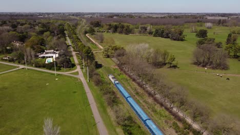 Blue-train-crossing-green-countryside-of-Buenos-Aires,-Argentine