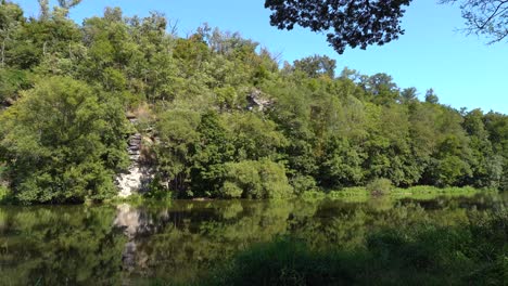 Ruhiger-Fluss-Sazava-Von-Seinem-Ufer-Mit-Einem-Felsen-Und-Einem-Wald-Im-Hintergrund