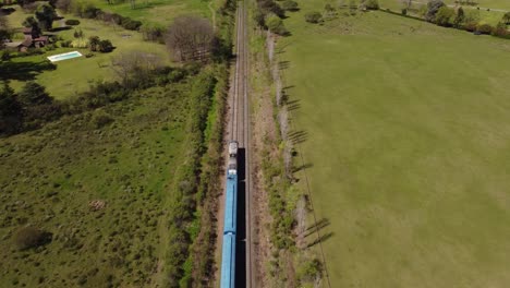 Aerial-tracking-shot-of-blue-train-driving-between-green-rural-landscape-of-Buenos-Aires