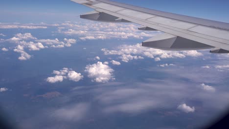 Looking-out-from-airplane-window-at-wing-and-partially-cloudy-sky