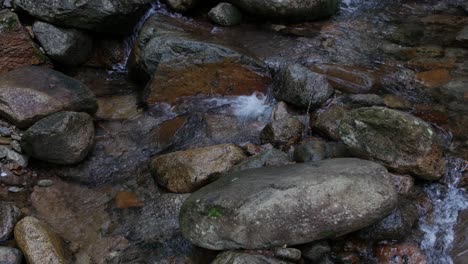 Calm-water-runs-over-various-colorful-rocks-as-the-camera-tilts-to-a-close-angle