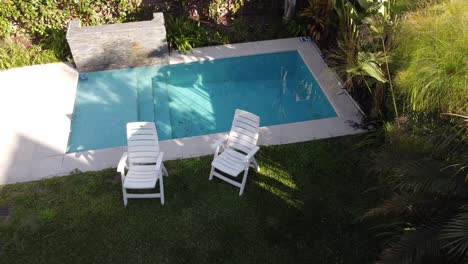 Drone-flying-up-over-a-Garden-with-plastic-chairs-and-swimming-pool