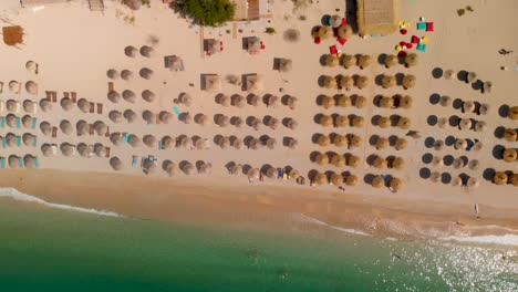 Slow-aerial-overhead-flight-over-many-umbrellas-and-waves-at-stunning-sand-beach