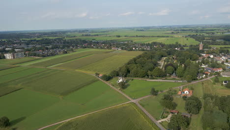 Aerial-of-spinning-windmill-surrounded-by-green-meadows-in-a-small-rural-town