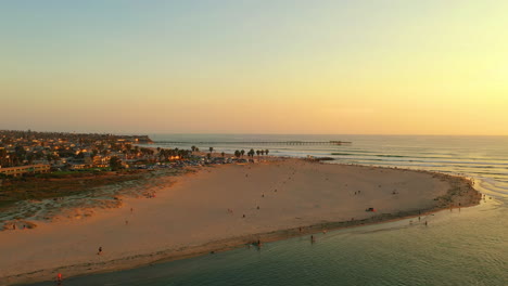 Drone-circles-around-dog-beach-in-Ocean-Beach,-San-Diego,-California-at-sunset