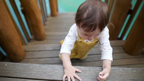 Cute-Asian-Ukrainian-girl-toddler-learning-to-climb-stairs-on-a-wooden-playground-set---slow-motion