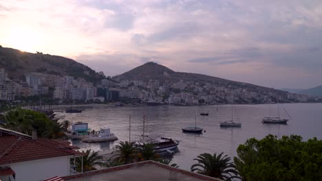 Early-morning-view-of-Saranda,-Albania-with-slowly-rising-sun-and-boats-in-harbor