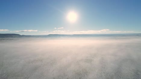 4k-Antenne-über-Verschneiter-Wüste,-Eingehüllt-In-Niedrigen-Nebel,-Der-Sich-Auf-Die-Aufgehende-Sonne-Zubewegt