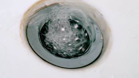 Soapy-Water-Flowing-Down-The-Drain-Of-A-Sink-In-The-Bathroom---high-angle,-close-up