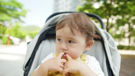 Adorable-Baby-Girl-With-Mixed-Ethnicity-Sucking-Fingers-While-Sitting-In-A-Stroller-Outdoor