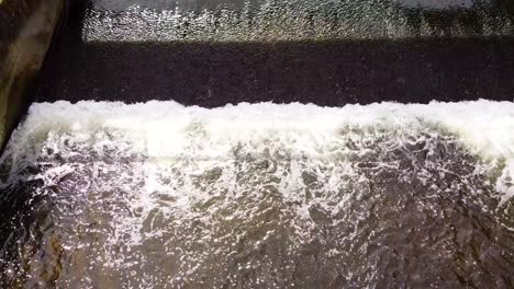 Aerial-top-down-slow-motion-shot-of-a-small-water-dam-on-the-Little-Ouse-river-near-Thetford-in-the-UK