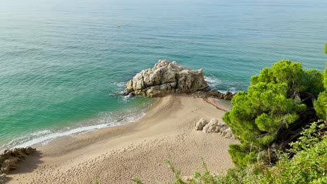 Hermosa-Playa-Paradisíaca-En-La-Costa-Mediterránea-Del-Maresme-Barcelona-Vista-Aérea-Agua-Azul-Turquesa-Con-Rocas-Naturales