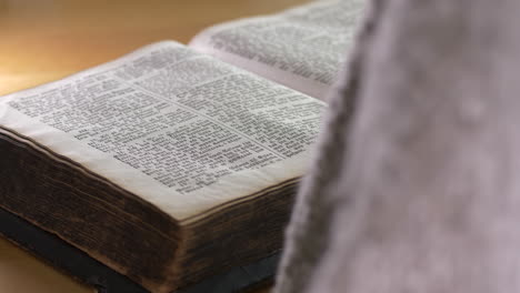 Person-sits-down-says-a-prayer-and-put-arms-on-bible-book,-close-up-back-view