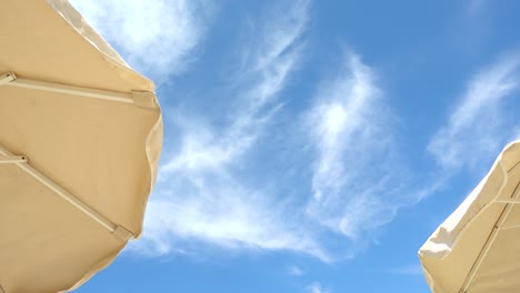 Looking-up-towards-two-beach-umbrellas-against-blue-sky-with-clouds