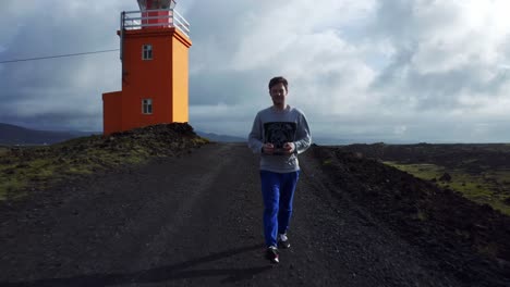 Man-With-Drone-Remote-Control-Walking-On-Trail-Near-Hopsnesviti-Lighthouse-On-Southwest-Coast-Of-Iceland