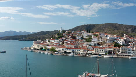 Flying-Towards-Waterfront-Houses-In-Poros-Island-With-Boats-In-The-Sea-In-Greece