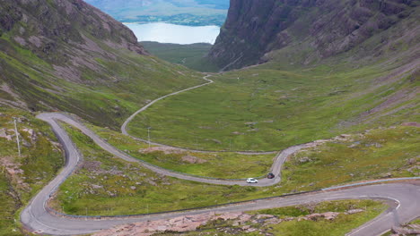 Revealing-drone-shot-two-vehicles-on-Bealach-Na-Ba-Applecross-road-through-the-mountains-of-the-Applecross-peninsula,-in-Wester-Ross-in-the-Scottish-Highlands