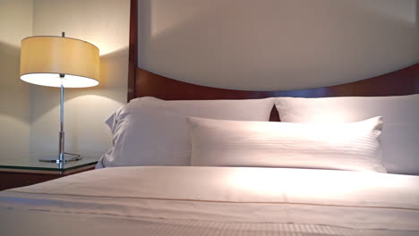 Slow-pan-right-on-the-made-up-king-sized-bed-with-white-striped-linen-pillows-and-cover-at-night-with-turned-on-Lamps-in-a-hotel-in-Houston,-USA