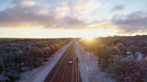 Aerial-of-beautiful-sunrise-remote-frozen-highway-as-car-passes-underneath,-4K