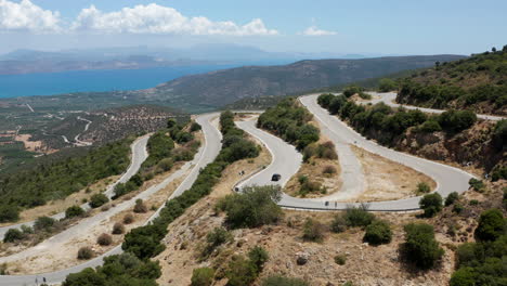 Car-Going-Down-On-A-Winding-Road-By-The-Mountain-On-A-Sunny-Summer-Day-In-Peloponnese,-Greece