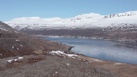 Eskifjörður-fjord-and-distant-village-seen-from-Holmanes-peninsula,-aerial