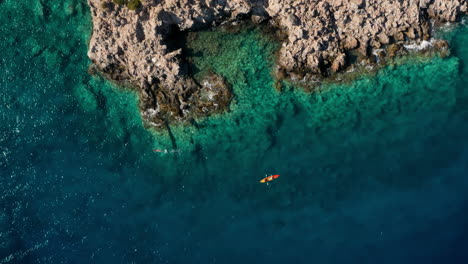 Tourist-Swimming-and-Kayaking-In-the-Beautiful-Pristine-Waters-By-the-Island-of-Crete-In-Greece---aerial-shot