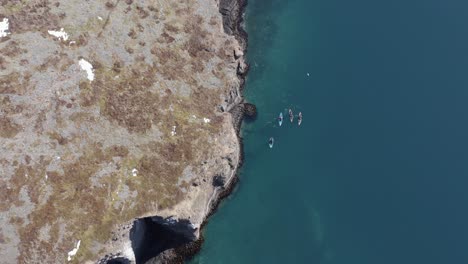 Four-kayakers-moving-along-wild-rugged-shore-of-Iceland-Holmanes-peninsula,-aerial