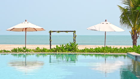 Luxuriöser-Tropischer-Pool,-Strandbogen,-Sonnenschirme-Und-Reflexion-über-Poolwasser-An-Sonnigen-Tagen,-Vollbild