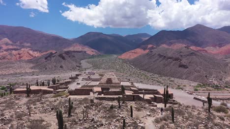Vista-Aérea-De-Un-Pequeño-Pueblo-Con-Un-Templo-Inca-En-Medio-De-Un-Valle-Montañoso-Y-Desértico-En-Jujuy,-Pucará-Argentina